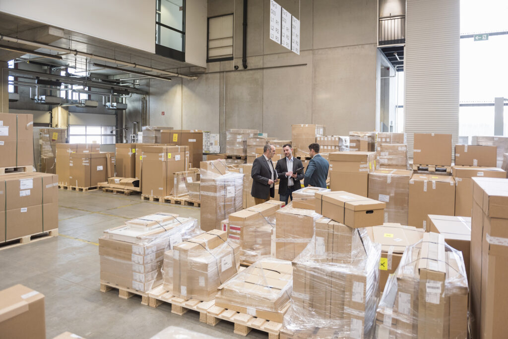 Three men in factory warehouse surrounded by cardboard boxes